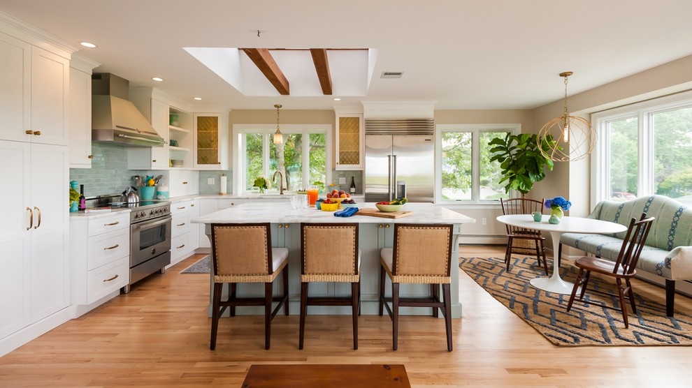 This is an example of a traditional l-shaped eat-in kitchen in Boston with shaker cabinets, white cabinets, blue splashback, subway tile splashback, stainless steel appliances, light hardwood floors and with island.