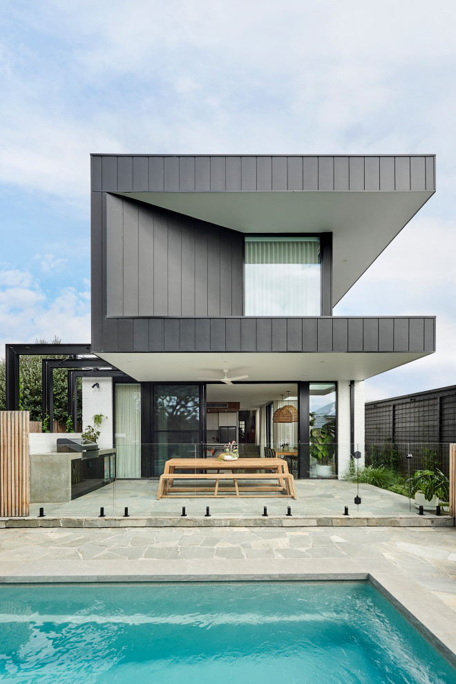 Cette image montre une façade de maison noire design de taille moyenne et à un étage avec un toit plat.