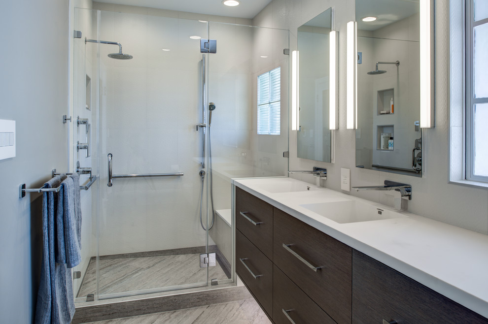 This is an example of a mid-sized modern master bathroom in San Francisco with an integrated sink, flat-panel cabinets, dark wood cabinets, solid surface benchtops, an alcove shower, a wall-mount toilet, gray tile, porcelain tile, grey walls, porcelain floors, grey floor, a hinged shower door, white benchtops, a niche, a double vanity and a floating vanity.