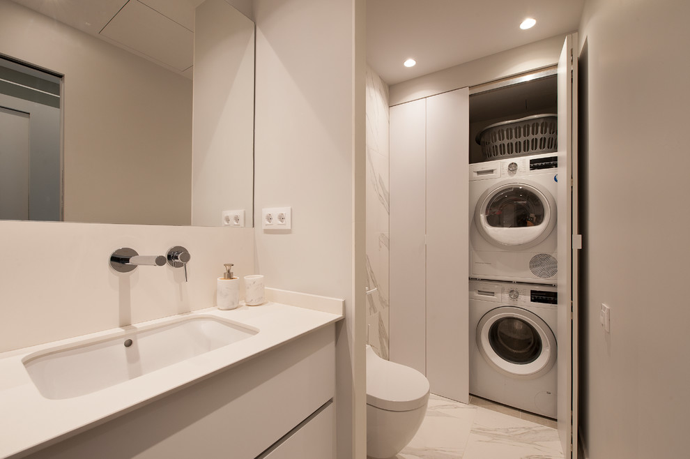 Photo of a small modern single-wall laundry cupboard in Other with recessed-panel cabinets, white cabinets, white walls, porcelain floors, a concealed washer and dryer and white floor.