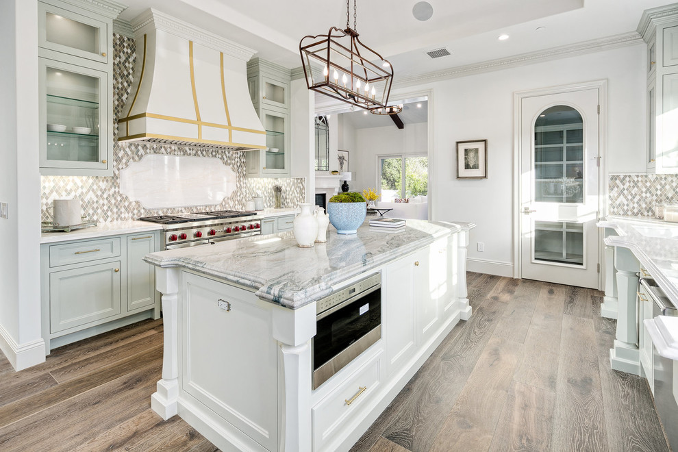 Traditional galley kitchen in Los Angeles with recessed-panel cabinets, grey cabinets, multi-coloured splashback, mosaic tile splashback, stainless steel appliances, dark hardwood floors, with island, brown floor and white benchtop.