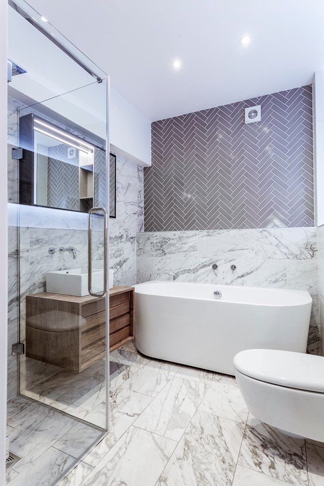 This is an example of a mid-sized contemporary 3/4 bathroom in London with flat-panel cabinets, brown cabinets, a hot tub, a shower/bathtub combo, a wall-mount toilet, multi-coloured tile, marble, marble floors, a pedestal sink, marble benchtops and white walls.