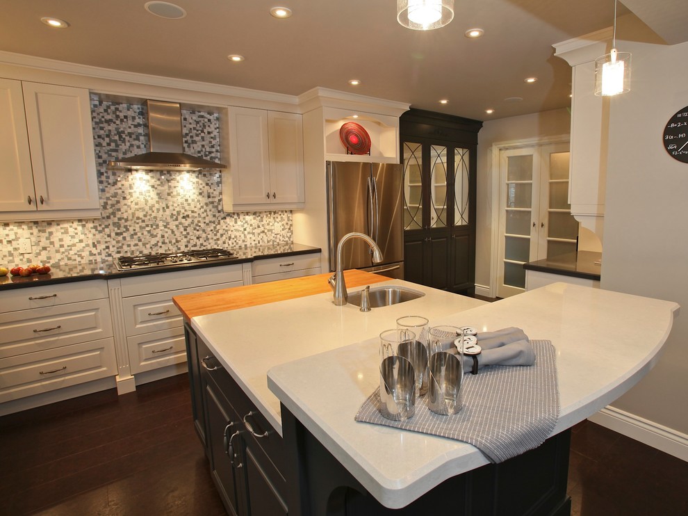 Example of a mid-sized transitional l-shaped medium tone wood floor eat-in kitchen design with an undermount sink, raised-panel cabinets, white cabinets, quartz countertops, multicolored backsplash, mosaic tile backsplash, stainless steel appliances and an island