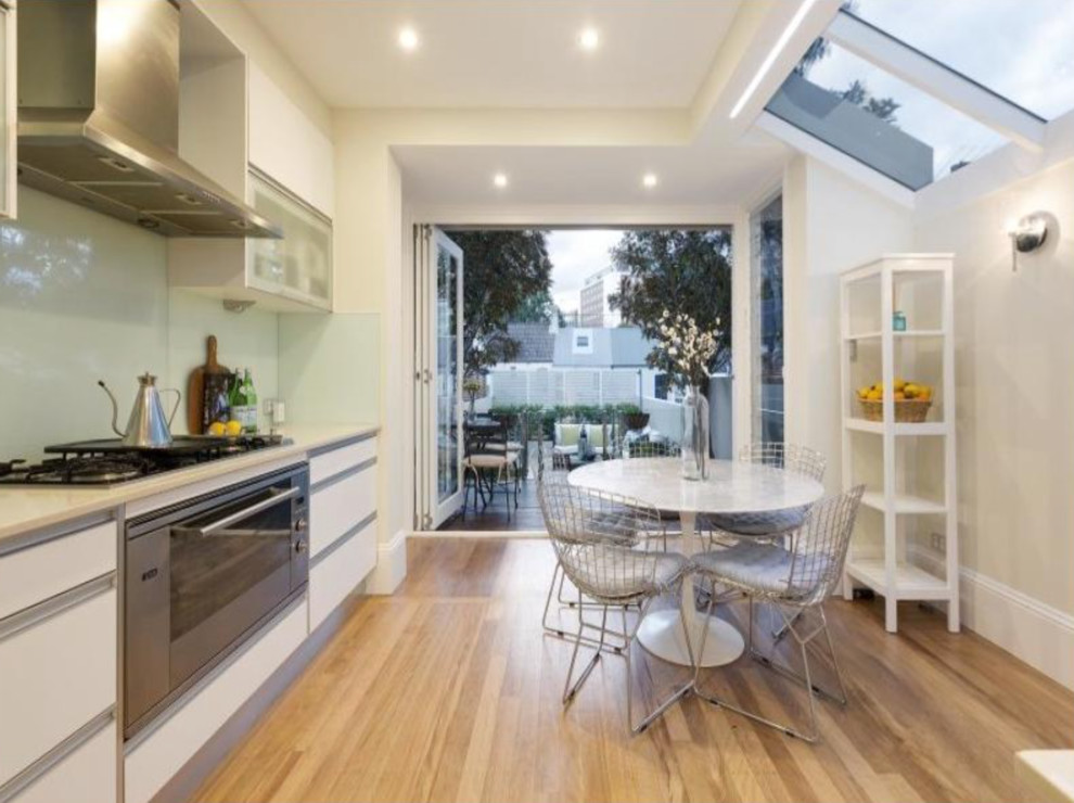 This is an example of a contemporary eat-in kitchen in Sydney with white cabinets, limestone benchtops, white splashback, ceramic splashback, stainless steel appliances, light hardwood floors and brown floor.