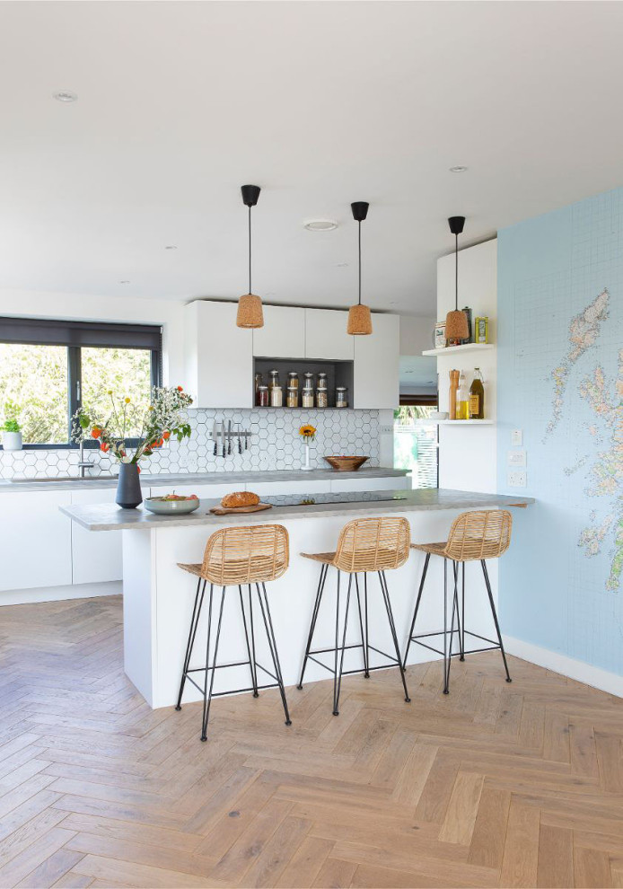Mid-sized scandinavian galley kitchen in Glasgow with a drop-in sink, flat-panel cabinets, white cabinets, concrete benchtops, white splashback, porcelain splashback, panelled appliances, light hardwood floors, a peninsula, beige floor and grey benchtop.