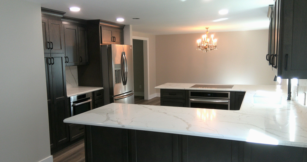 This is an example of a mid-sized traditional u-shaped eat-in kitchen in Detroit with an undermount sink, recessed-panel cabinets, dark wood cabinets, quartzite benchtops, white splashback, stainless steel appliances, vinyl floors, a peninsula, beige floor and white benchtop.