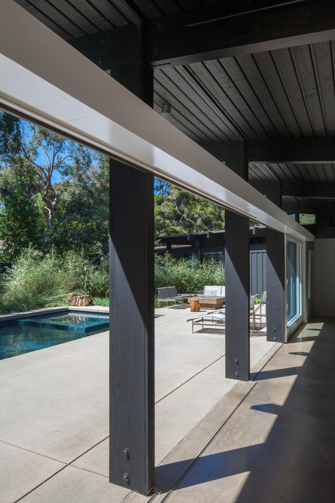 Large midcentury backyard rectangular lap pool in Los Angeles with concrete slab.