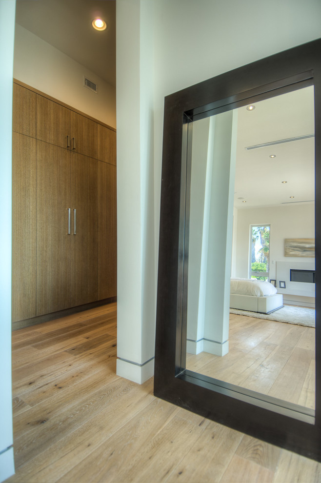 This is an example of a large contemporary gender-neutral walk-in wardrobe in Los Angeles with medium wood cabinets and light hardwood floors.