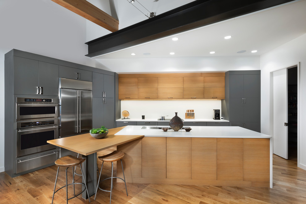 Mid-sized contemporary l-shaped open plan kitchen in Other with flat-panel cabinets, grey cabinets, quartz benchtops, white splashback, stainless steel appliances, medium hardwood floors, with island and brown floor.