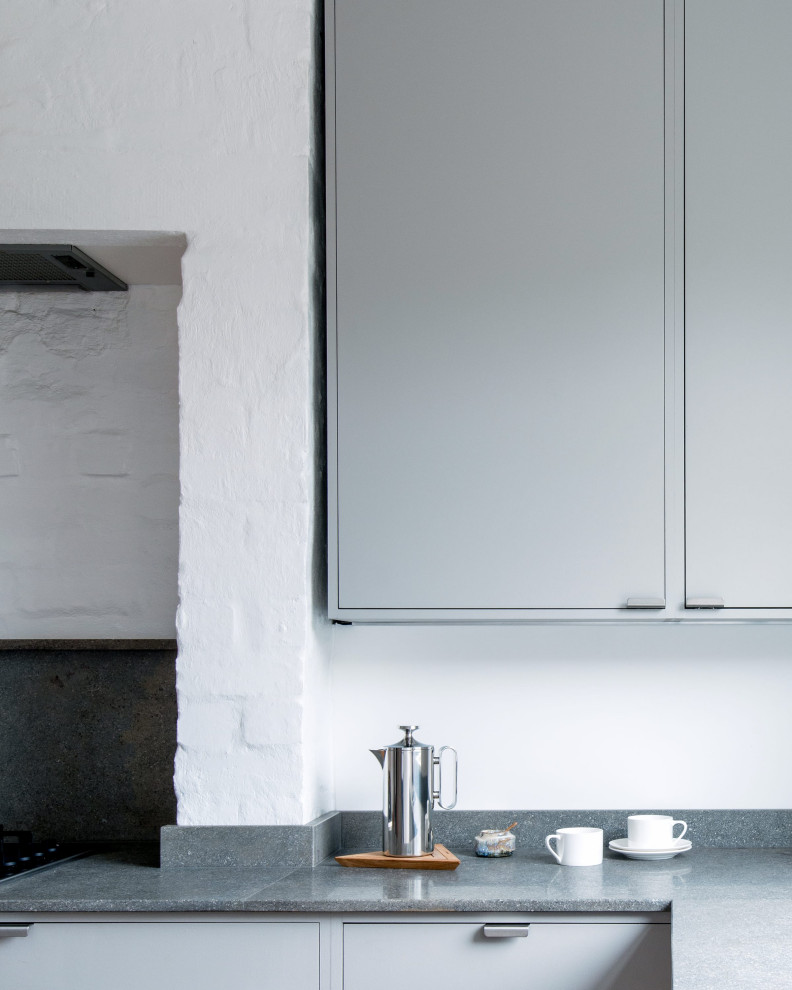 Small contemporary l-shaped kitchen/diner in London with a double-bowl sink, flat-panel cabinets, grey cabinets, limestone worktops, grey splashback, limestone splashback, stainless steel appliances, cork flooring, no island, grey worktops and a chimney breast.