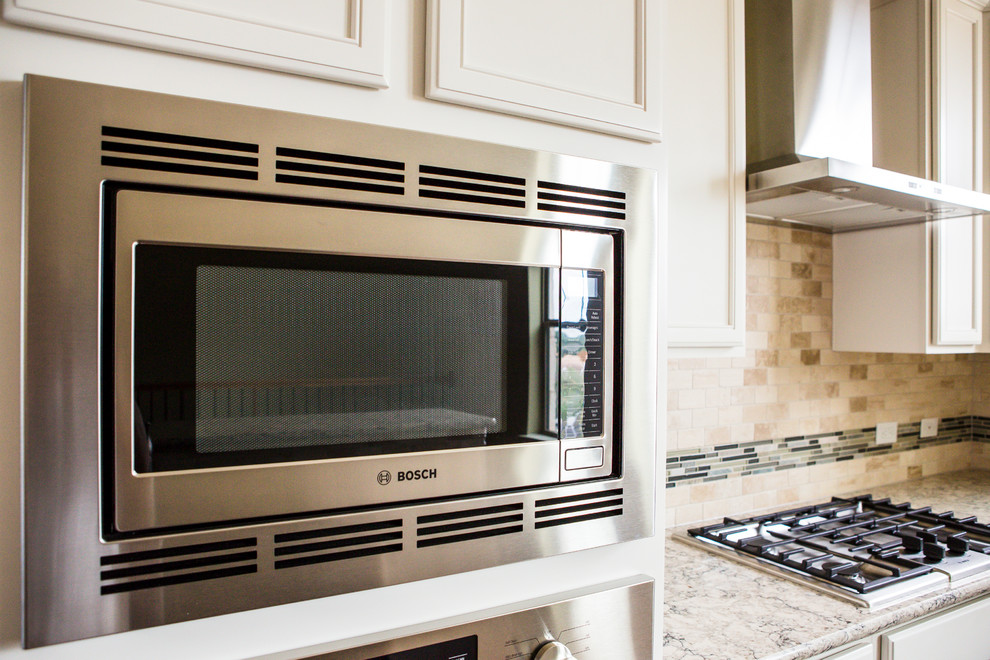 Mid-sized transitional l-shaped medium tone wood floor eat-in kitchen photo in Austin with an undermount sink, recessed-panel cabinets, white cabinets, granite countertops, beige backsplash, stone tile backsplash, stainless steel appliances and an island