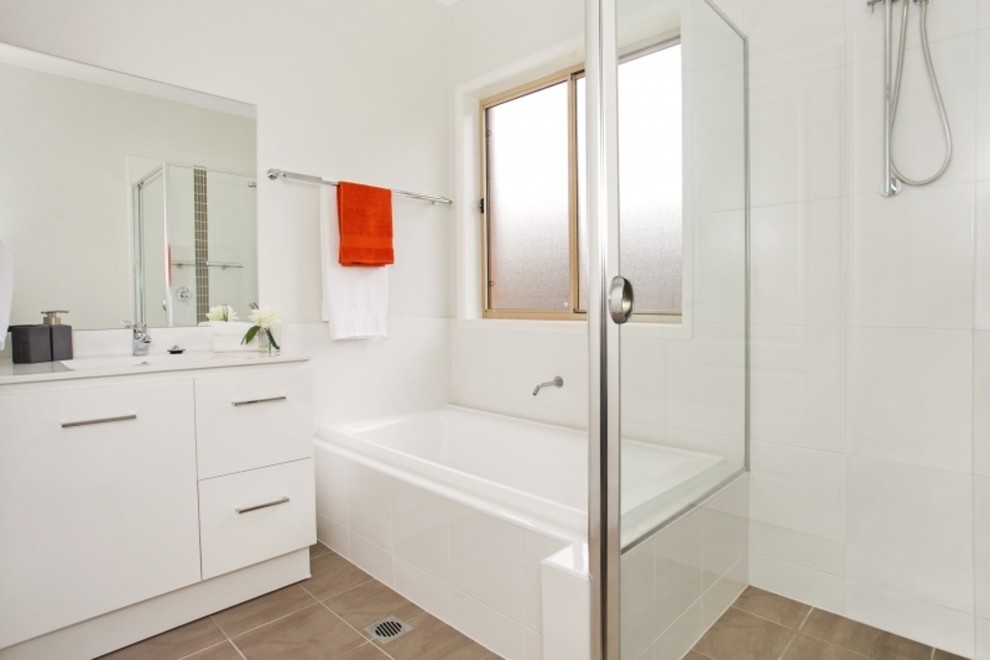 Photo of a small modern 3/4 bathroom in Newcastle - Maitland with a drop-in sink, recessed-panel cabinets, white cabinets, solid surface benchtops, a drop-in tub, a corner shower, a one-piece toilet, white tile, ceramic tile, white walls, ceramic floors and a hinged shower door.