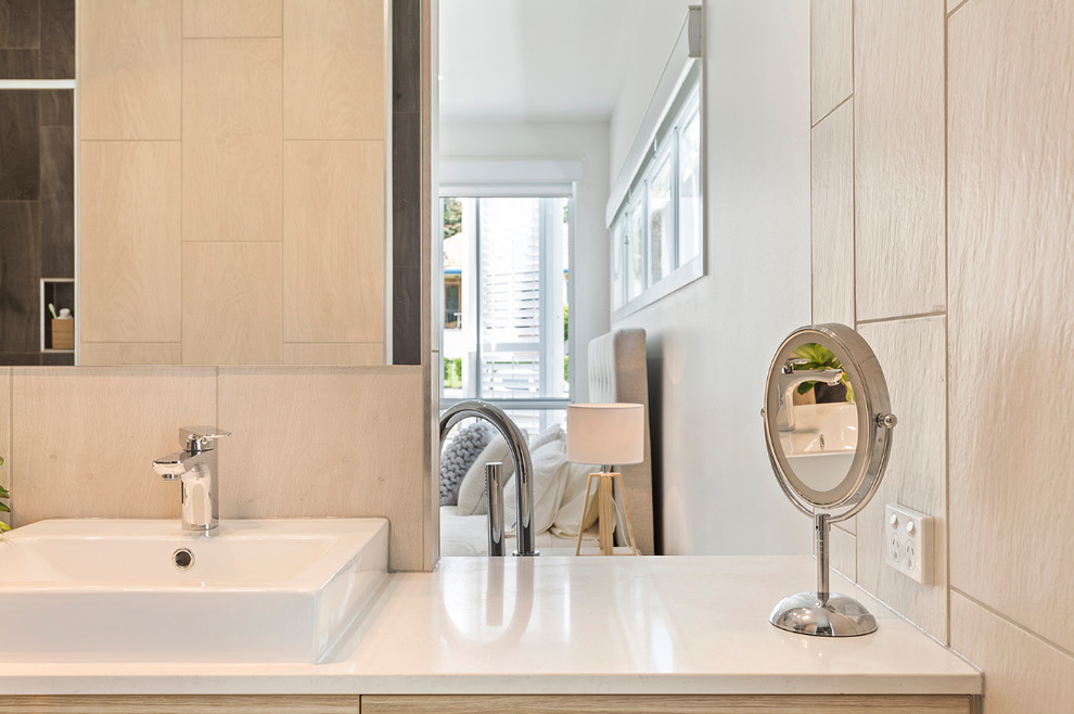 Photo of a large modern master bathroom in Brisbane with light wood cabinets, beige tile, ceramic tile, an alcove shower, beige walls, ceramic floors, an integrated sink, beige floor, a hinged shower door, furniture-like cabinets, a freestanding tub, a two-piece toilet and engineered quartz benchtops.