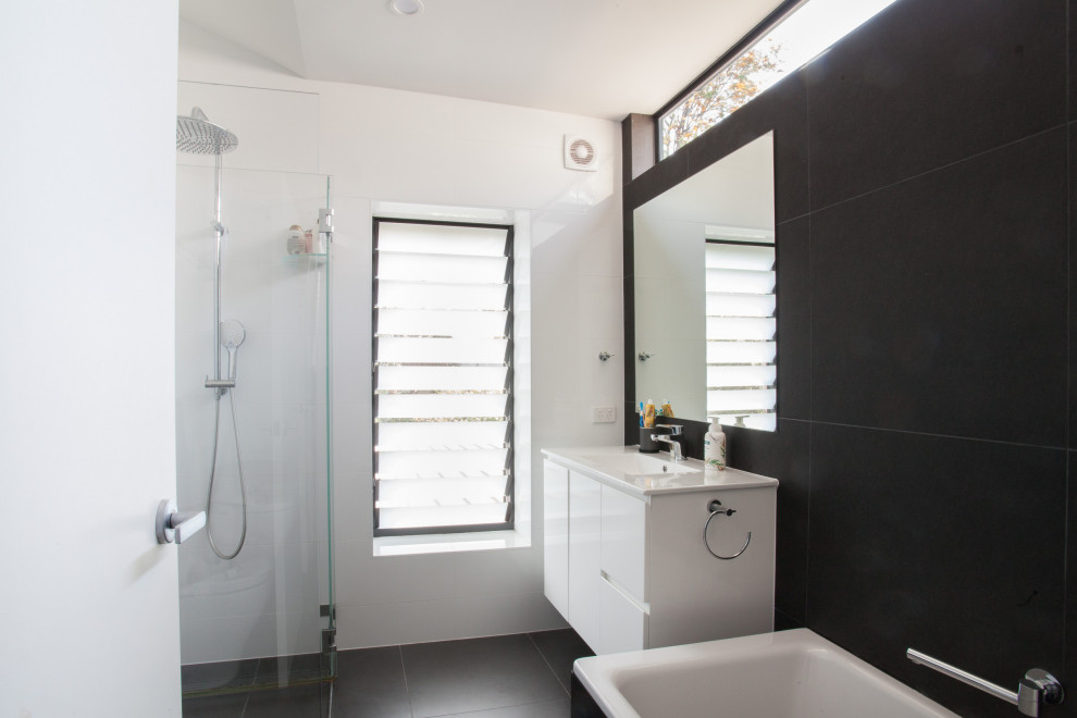 Photo of a mid-sized modern master bathroom in Sydney with white cabinets, a drop-in tub, an open shower, a one-piece toilet, black and white tile, ceramic tile, black walls, ceramic floors, a drop-in sink, solid surface benchtops, grey floor, a hinged shower door and white benchtops.