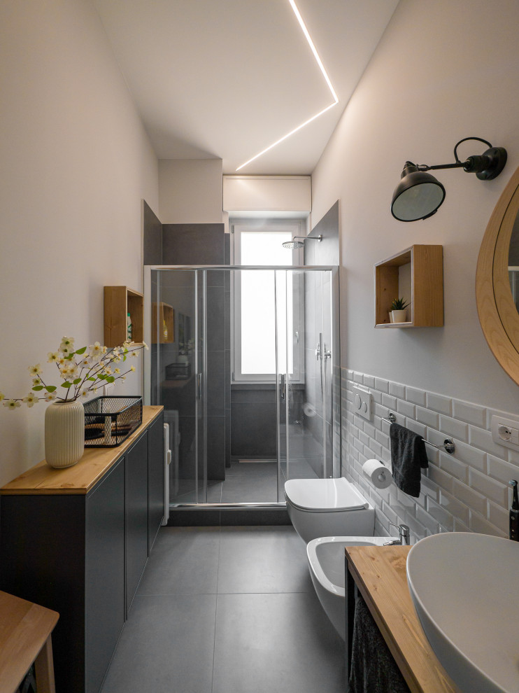 Inspiration for a mid-sized industrial 3/4 bathroom in Milan with open cabinets, light wood cabinets, an alcove shower, a two-piece toilet, white tile, porcelain tile, grey walls, porcelain floors, a vessel sink, wood benchtops, grey floor, a sliding shower screen, a single vanity, a freestanding vanity and recessed.