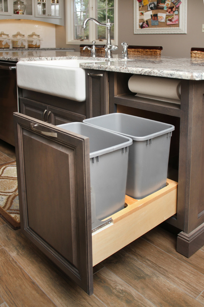 Large transitional l-shaped porcelain tile eat-in kitchen photo with a farmhouse sink, granite countertops, white backsplash, ceramic backsplash, stainless steel appliances, an island, recessed-panel cabinets and gray cabinets