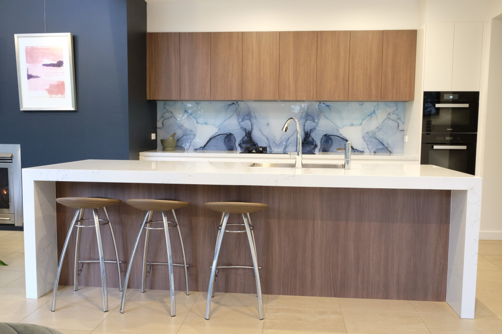 Design ideas for a mid-sized contemporary single-wall open plan kitchen in Sydney with an undermount sink, flat-panel cabinets, medium wood cabinets, quartz benchtops, blue splashback, glass sheet splashback, black appliances, ceramic floors, with island, beige floor and white benchtop.