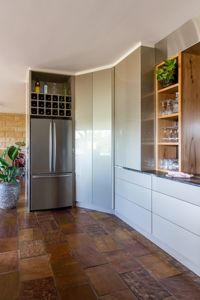 Large modern u-shaped kitchen pantry in Central Coast with a double-bowl sink, flat-panel cabinets, beige cabinets, granite benchtops, metallic splashback, glass sheet splashback, stainless steel appliances, slate floors, a peninsula, brown floor and black benchtop.