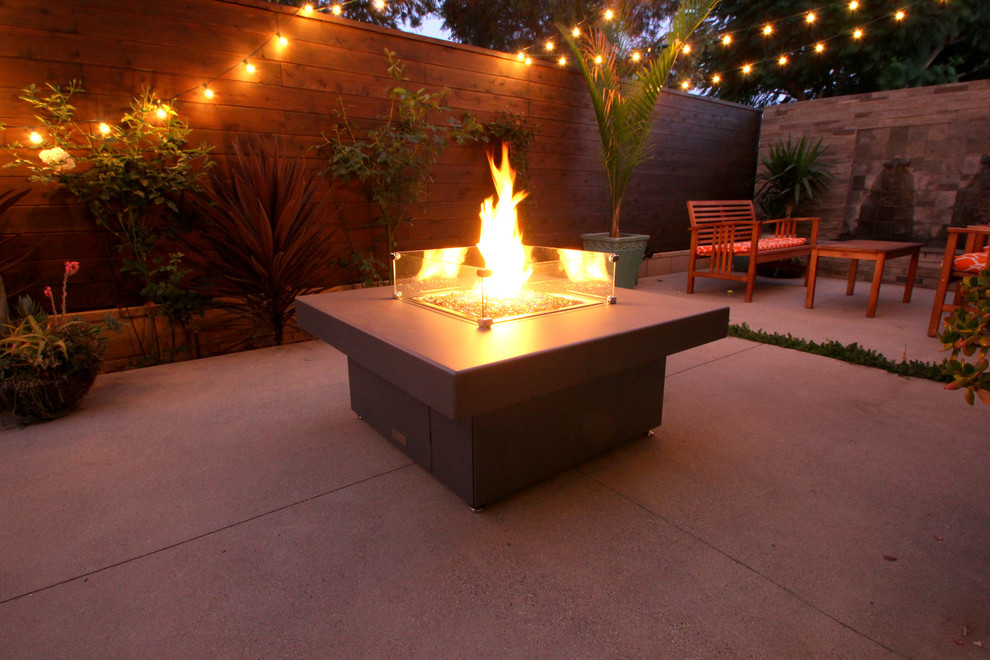 This is an example of a mid-sized tropical backyard patio in Orange County with a fire feature, concrete slab and no cover.