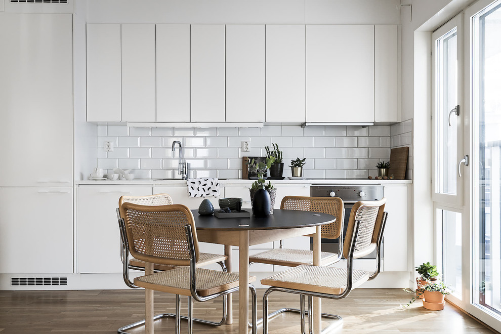 Photo of a small scandinavian single-wall eat-in kitchen in Stockholm with flat-panel cabinets, white cabinets, subway tile splashback, white appliances, no island, beige floor, white benchtop, white splashback and light hardwood floors.