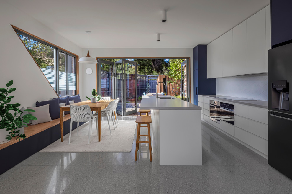 This is an example of a mid-sized contemporary single-wall open plan kitchen in Melbourne with an undermount sink, blue cabinets, grey splashback, ceramic splashback, black appliances, concrete floors, with island, grey floor and grey benchtop.