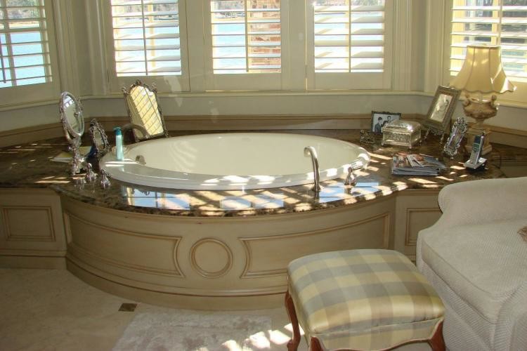 Beige tile porcelain tile bathroom photo with white cabinets, granite countertops and a hot tub