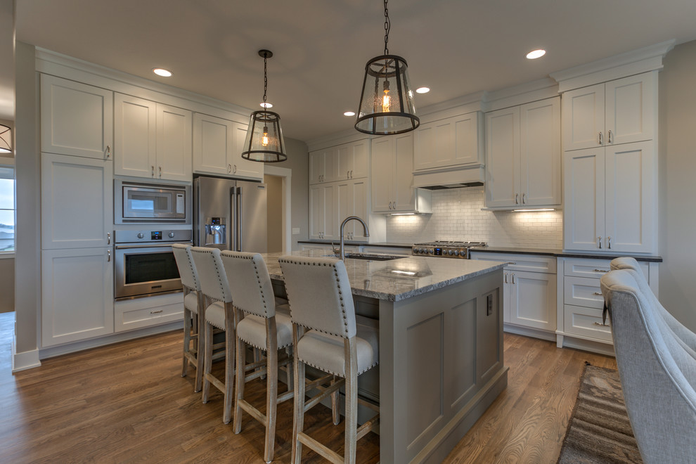 Eat-in kitchen - mid-sized transitional l-shaped medium tone wood floor and beige floor eat-in kitchen idea in Omaha with an undermount sink, recessed-panel cabinets, white cabinets, granite countertops, white backsplash, subway tile backsplash, stainless steel appliances and an island