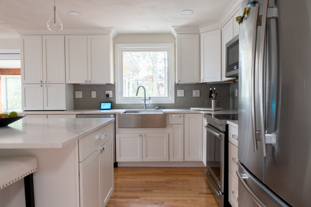Mid-sized transitional l-shaped light wood floor and brown floor eat-in kitchen photo in Boston with a farmhouse sink, shaker cabinets, white cabinets, quartz countertops, gray backsplash, ceramic backsplash, stainless steel appliances, an island and white countertops
