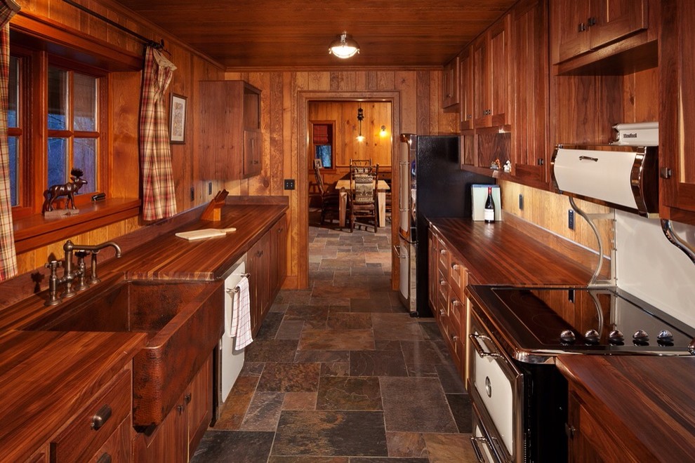 Photo of a mid-sized country galley separate kitchen in Other with an undermount sink, recessed-panel cabinets, medium wood cabinets, wood benchtops, brown splashback, white appliances and slate floors.