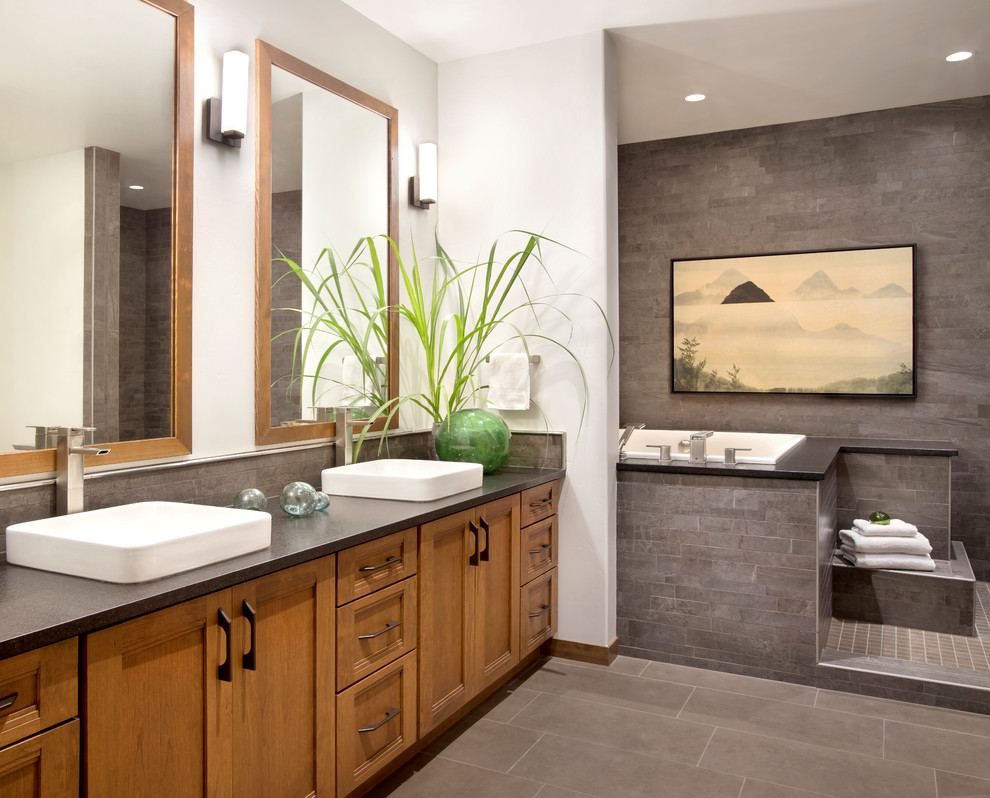 This is an example of a country master bathroom in Other with a vessel sink, recessed-panel cabinets, medium wood cabinets, a drop-in tub, gray tile and grey floor.