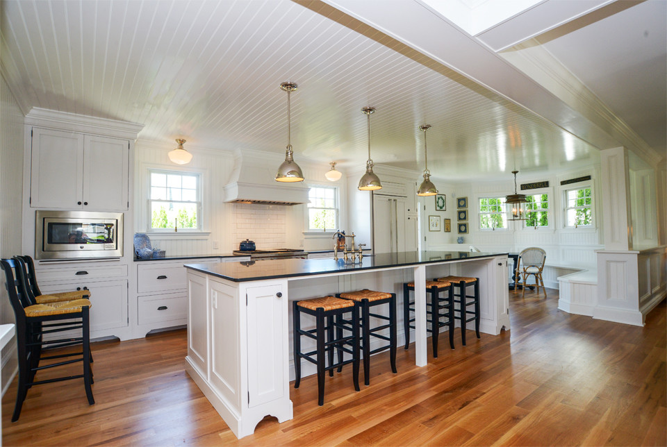 Inspiration for a large beach style galley open plan kitchen in Philadelphia with a farmhouse sink, shaker cabinets, white cabinets, quartz benchtops, white splashback, porcelain splashback, stainless steel appliances, medium hardwood floors and with island.
