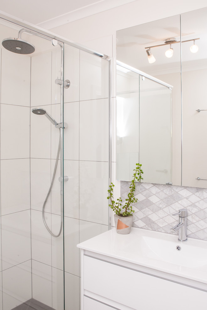 This is an example of a small contemporary bathroom in Melbourne with an integrated sink, white cabinets, solid surface benchtops, white tile, stone tile, white walls and a curbless shower.