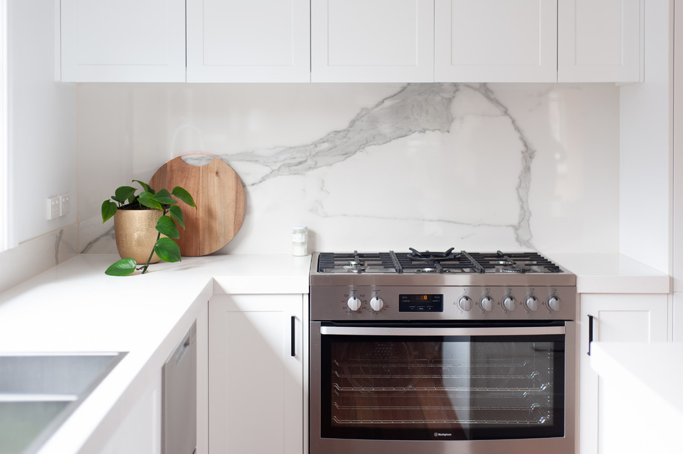 Photo of a large transitional u-shaped kitchen pantry in Melbourne with an undermount sink, recessed-panel cabinets, white cabinets, white splashback, stone slab splashback, stainless steel appliances, medium hardwood floors, with island and white benchtop.