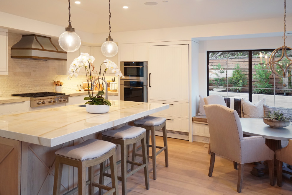 Small l-shaped eat-in kitchen in Orange County with an undermount sink, raised-panel cabinets, white cabinets, glass benchtops, white splashback, stone tile splashback, stainless steel appliances, light hardwood floors, with island, beige floor and beige benchtop.