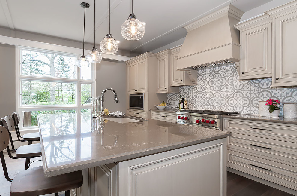 This is an example of a large traditional single-wall open plan kitchen in Chicago with an undermount sink, raised-panel cabinets, beige cabinets, granite benchtops, multi-coloured splashback, ceramic splashback, stainless steel appliances, medium hardwood floors, with island and brown floor.