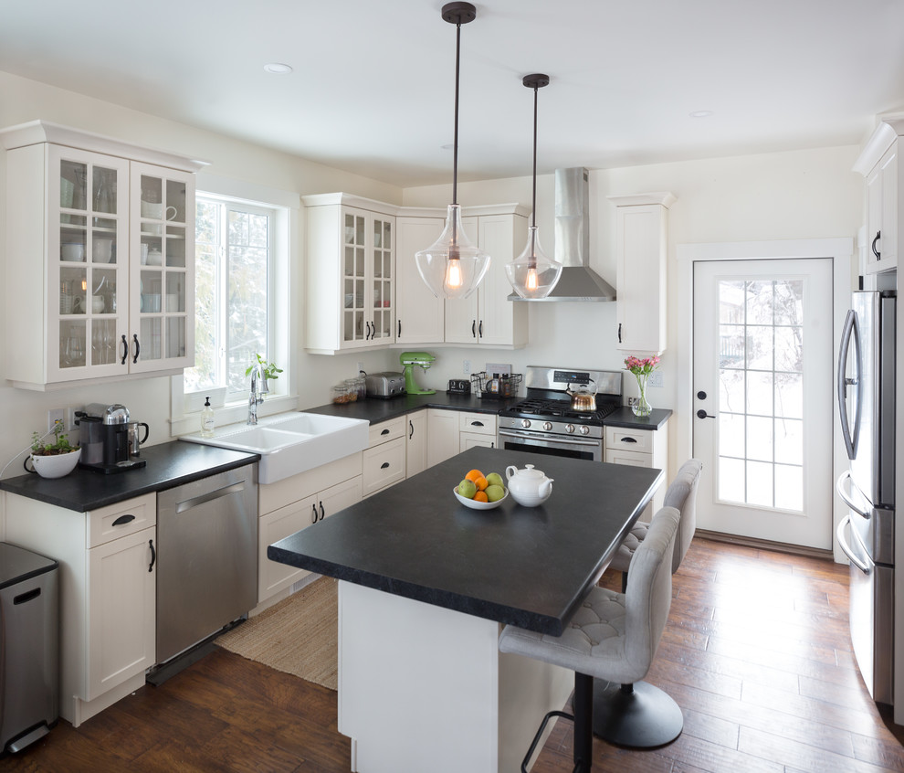 Design ideas for a country u-shaped kitchen in Other with a double-bowl sink, glass-front cabinets, white cabinets, laminate benchtops, stainless steel appliances, medium hardwood floors, with island, brown floor and black benchtop.