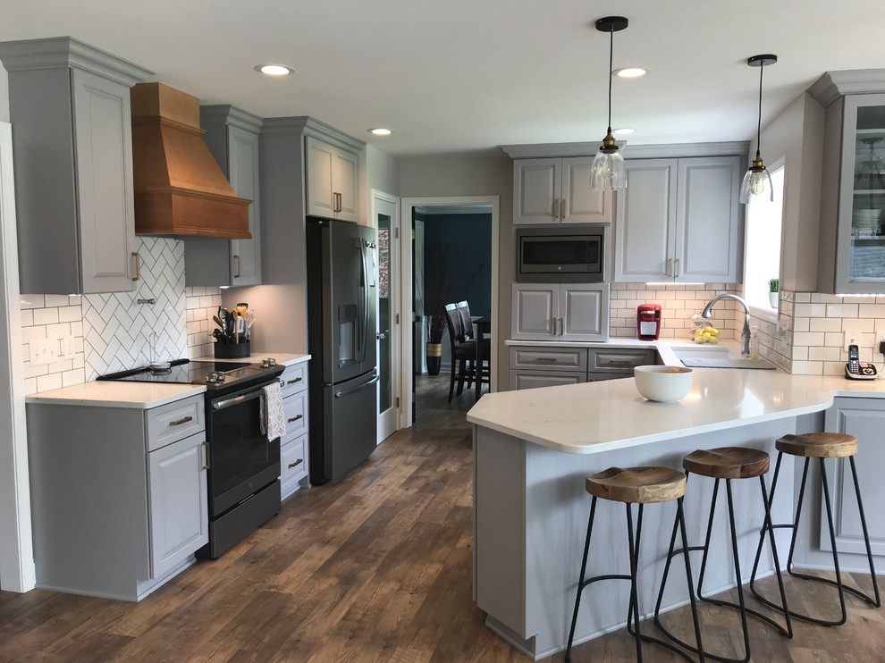 Mid-sized transitional u-shaped vinyl floor and brown floor enclosed kitchen photo with an undermount sink, raised-panel cabinets, gray cabinets, quartz countertops, white backsplash, ceramic backsplash, a peninsula and white countertops