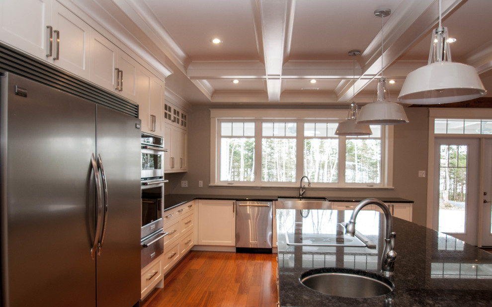 Example of a transitional dark wood floor kitchen design with a farmhouse sink, shaker cabinets, white cabinets, granite countertops and stainless steel appliances