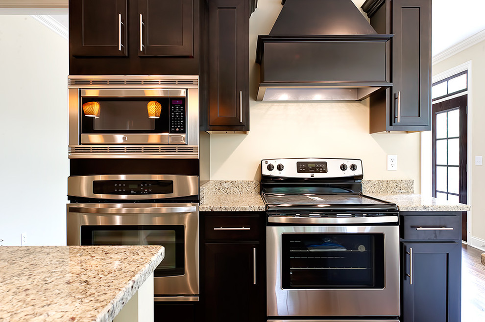 Transitional u-shaped medium tone wood floor eat-in kitchen photo with an undermount sink, recessed-panel cabinets, dark wood cabinets, granite countertops and an island