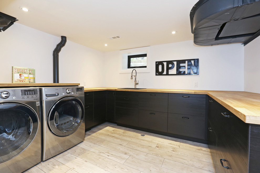 Large scandinavian u-shaped dedicated laundry room in Toronto with a drop-in sink, flat-panel cabinets, dark wood cabinets, wood benchtops, white walls, light hardwood floors and a side-by-side washer and dryer.