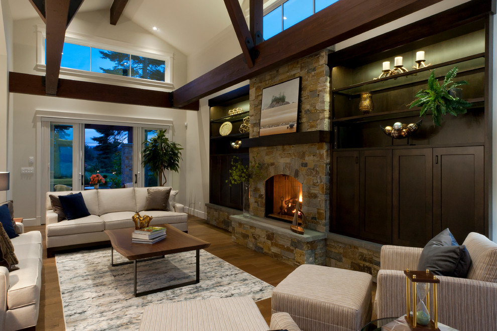 This is an example of an expansive beach style open concept living room in Vancouver with medium hardwood floors, a standard fireplace, a stone fireplace surround and a built-in media wall.