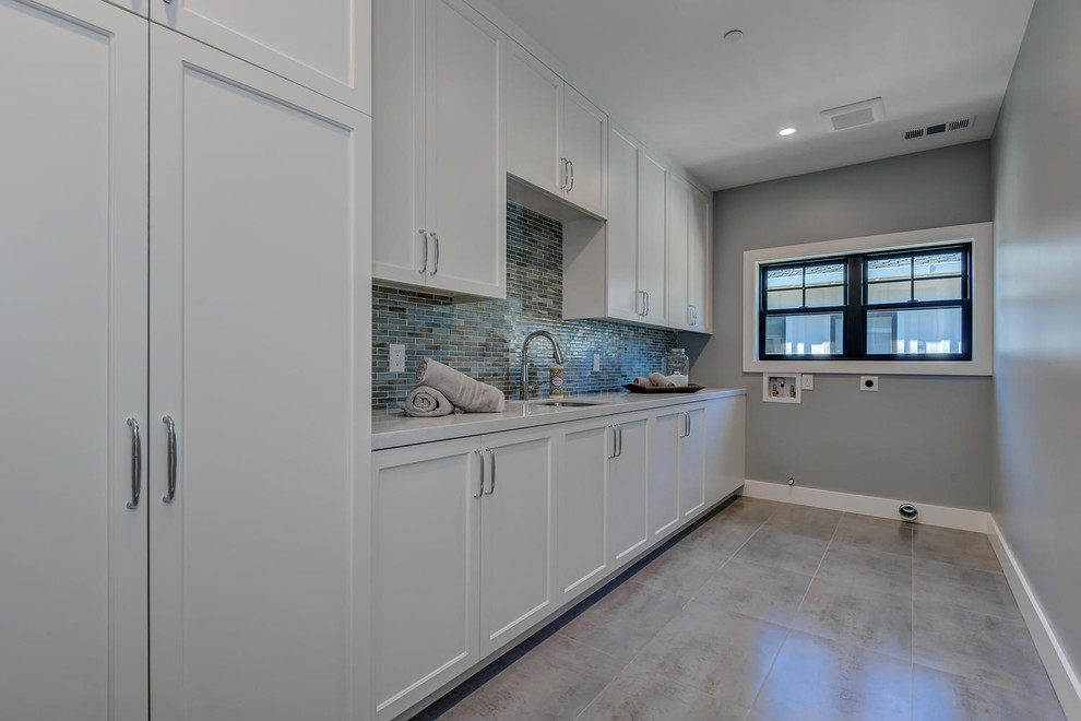 This is an example of a large transitional galley dedicated laundry room in San Francisco with an undermount sink, recessed-panel cabinets, white cabinets, quartzite benchtops, grey walls, porcelain floors, a side-by-side washer and dryer, grey floor and white benchtop.