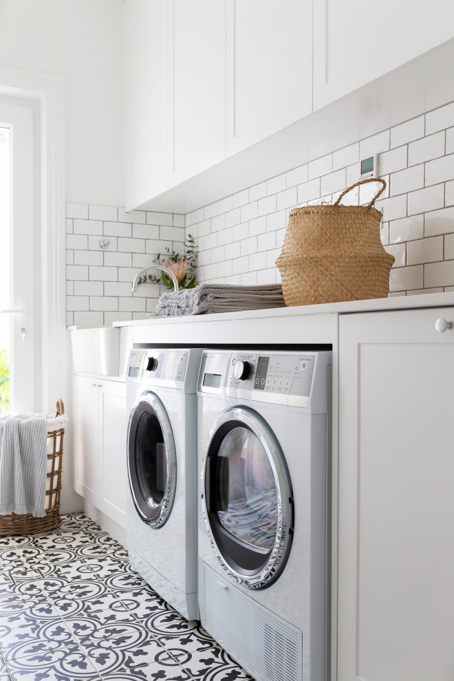 Design ideas for a mid-sized traditional galley laundry room in Canberra - Queanbeyan with a farmhouse sink, shaker cabinets, white cabinets, quartz benchtops, white splashback, subway tile splashback, porcelain floors, a side-by-side washer and dryer and white benchtop.