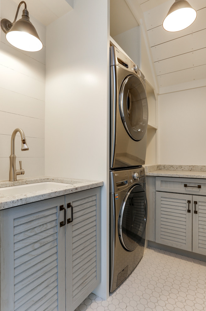 Inspiration for a small country dedicated laundry room in Raleigh with an undermount sink, louvered cabinets, grey cabinets, quartz benchtops, white walls, ceramic floors, a stacked washer and dryer, white floor and white benchtop.