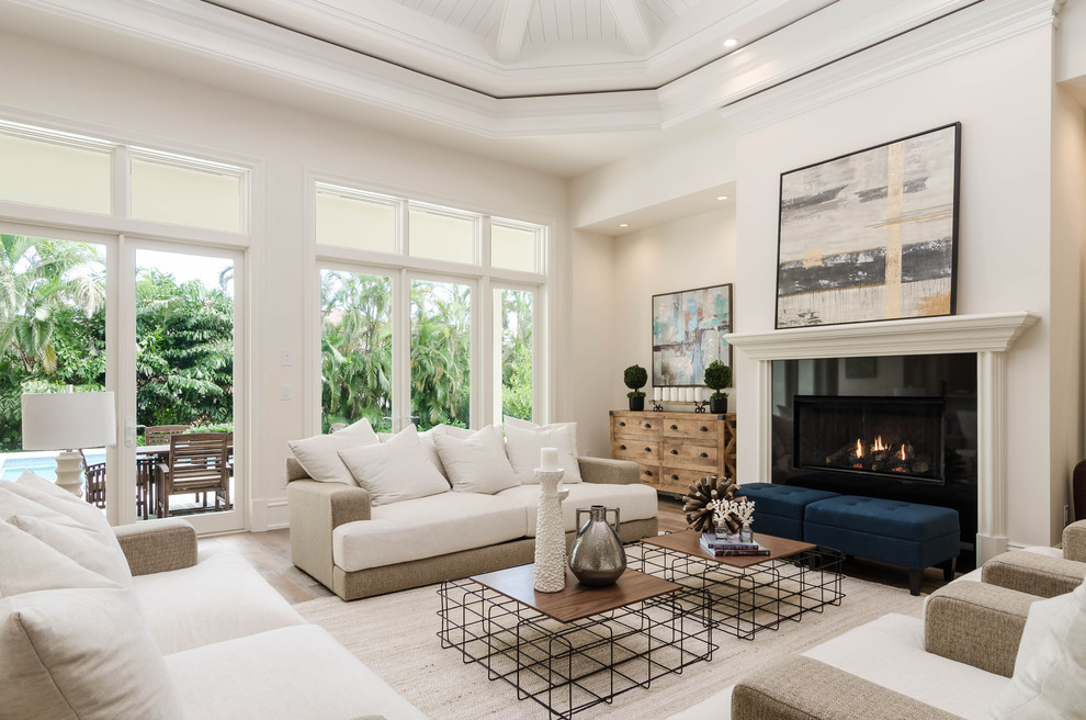 This is an example of a large transitional formal open concept living room in Miami with white walls, a standard fireplace, brown floor, medium hardwood floors, a wood fireplace surround and no tv.