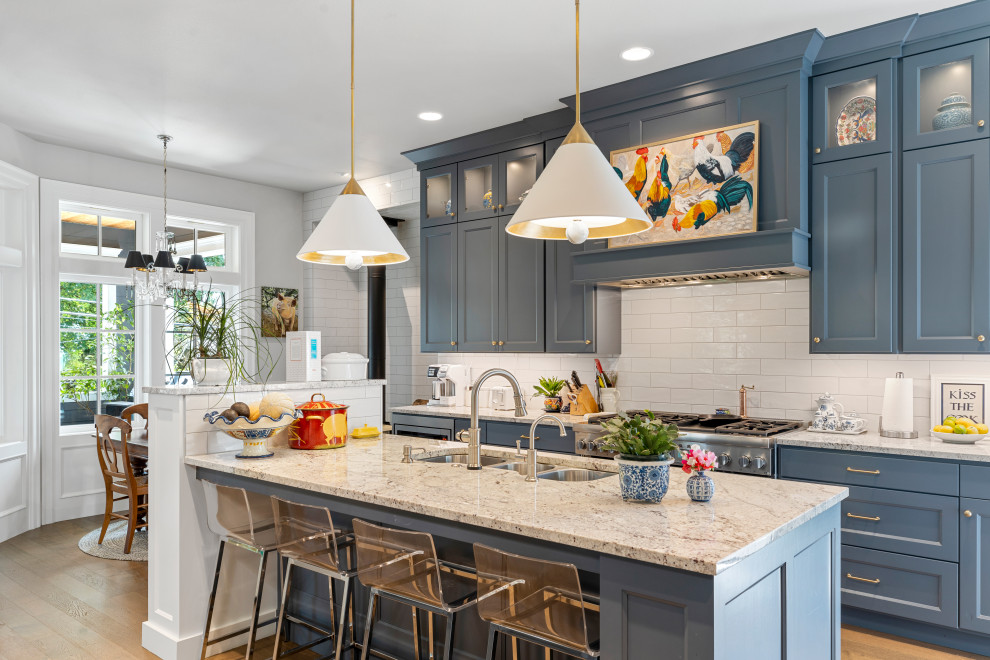 Photo of a mid-sized traditional galley eat-in kitchen in Portland with an undermount sink, recessed-panel cabinets, blue cabinets, quartz benchtops, white splashback, porcelain splashback, stainless steel appliances, medium hardwood floors, multiple islands, brown floor and white benchtop.
