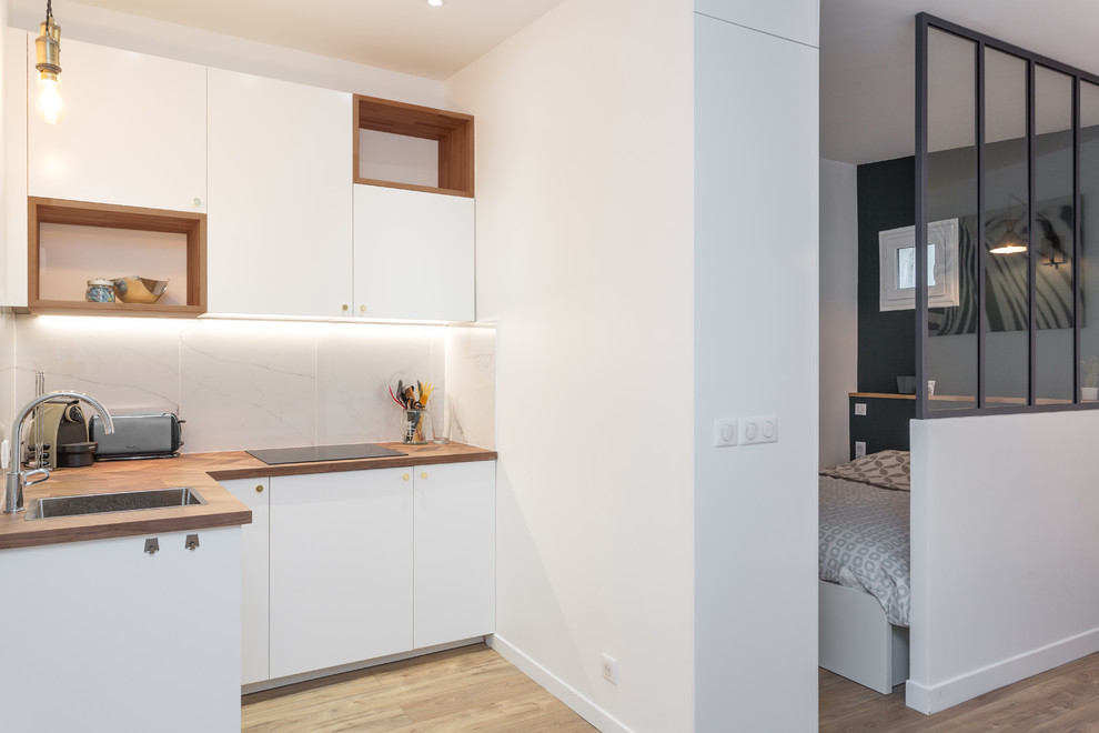 Mid-sized contemporary l-shaped open plan kitchen in Paris with white splashback, light hardwood floors, no island, white cabinets, wood benchtops, beige floor, a drop-in sink, flat-panel cabinets, marble splashback, panelled appliances and brown benchtop.
