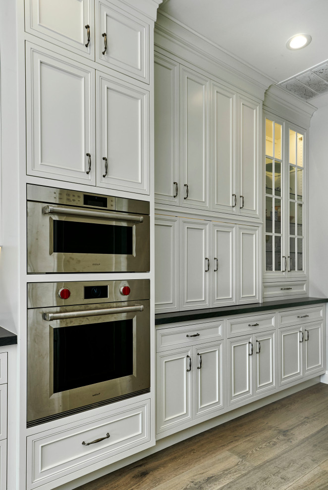 Bild på ett stort vintage vit vitt kök, med en rustik diskho, luckor med profilerade fronter, vita skåp, bänkskiva i onyx, vitt stänkskydd, integrerade vitvaror, ljust trägolv, flera köksöar och flerfärgat golv