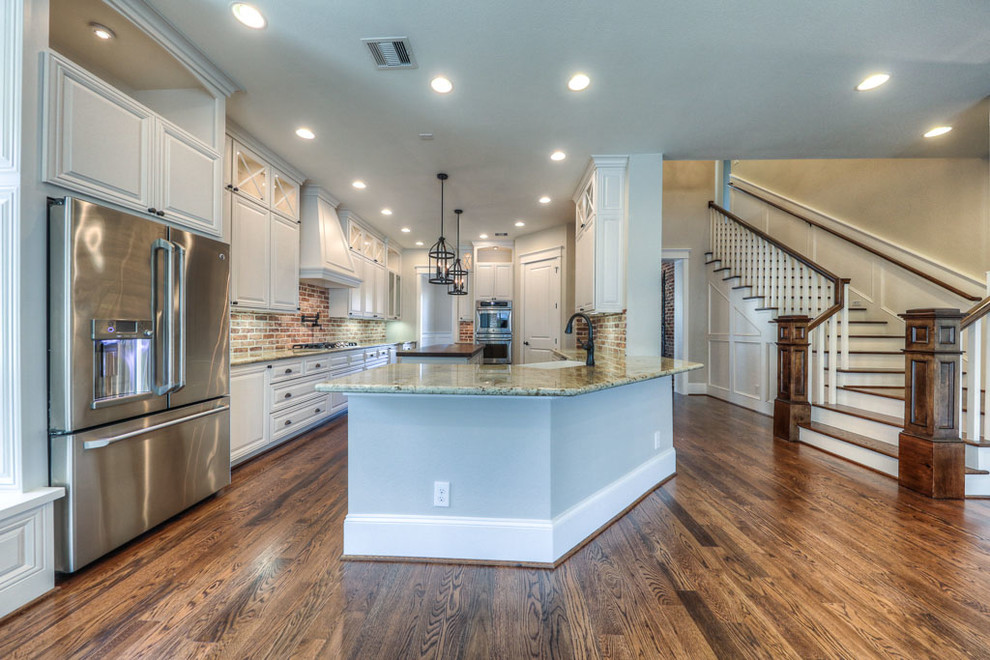 Photo of a large arts and crafts galley open plan kitchen in Houston with a farmhouse sink, raised-panel cabinets, white cabinets, wood benchtops, red splashback, stone tile splashback, stainless steel appliances, dark hardwood floors and with island.