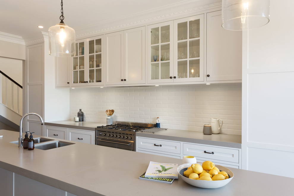 Photo of a large beach style galley open plan kitchen in Sydney with a double-bowl sink, flat-panel cabinets, white cabinets, white splashback, subway tile splashback, stainless steel appliances and dark hardwood floors.